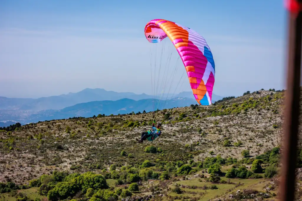 Pilote sous une BGD KISS 2 couleur Flamingo en vol au-dessus d’un relief montagneux rocheux