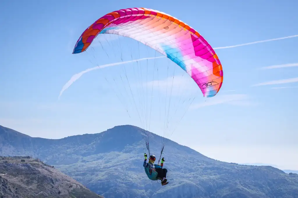 Pilote sous une BGD KISS 2 colorée en vol au-dessus d’une forêt